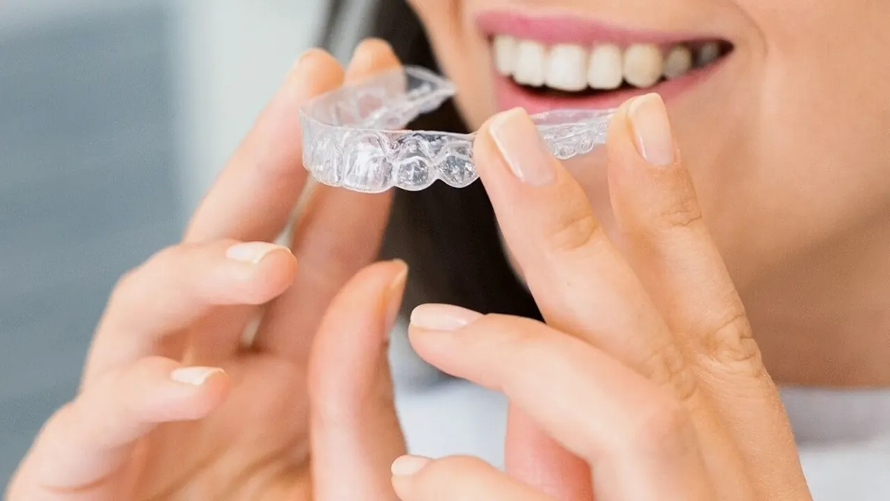 A patient holding a clear aligner in front of her smile